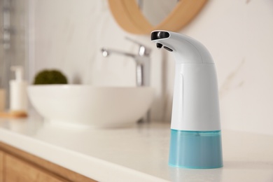 Modern automatic soap dispenser on countertop in bathroom. Space for text