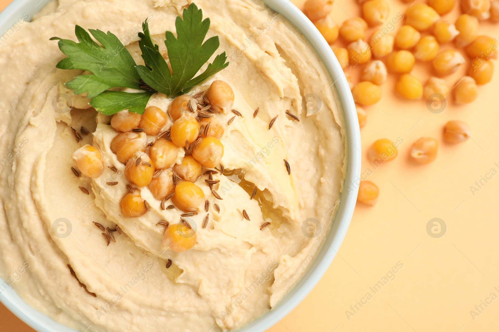 Bowl of tasty hummus with chickpeas and parsley on beige background, top view Photo of Bowl of tasty hummus with chickpeas and parsley on beige background, top view