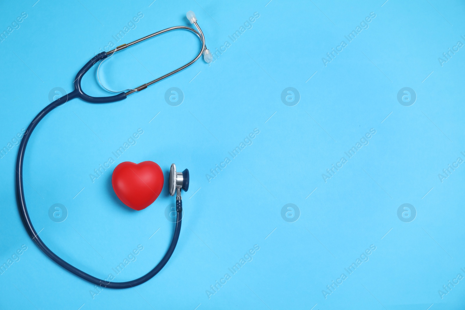 Photo of Stethoscope and red heart on light blue background, flat lay. Space for text