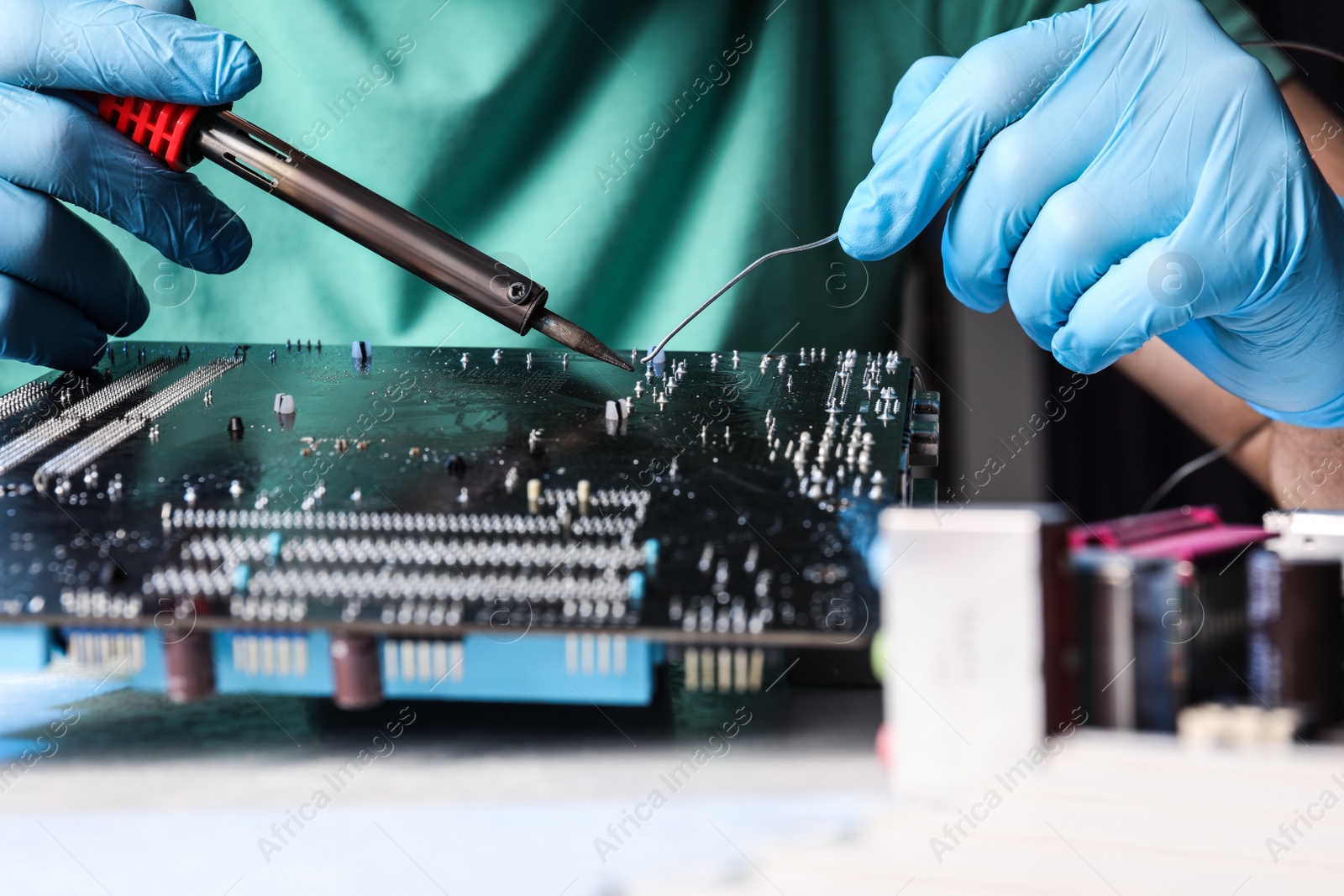 Photo of Technician repairing electronic circuit board with soldering iron at table, closeup