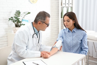 Photo of Young woman visiting doctor in hospital. Measuring blood pressure and checking pulse