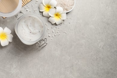 Body scrub, sea salt and plumeria flowers on grey table, flat lay. Space for text
