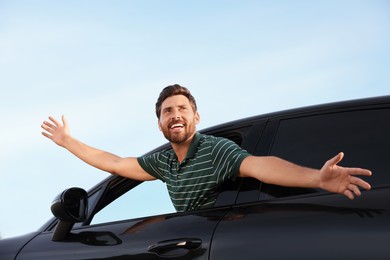 Enjoying trip. Happy man leaning out of car window outdoors, low angle view