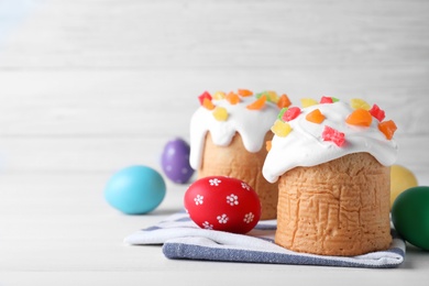 Photo of Easter cakes and color eggs on white table, space for text