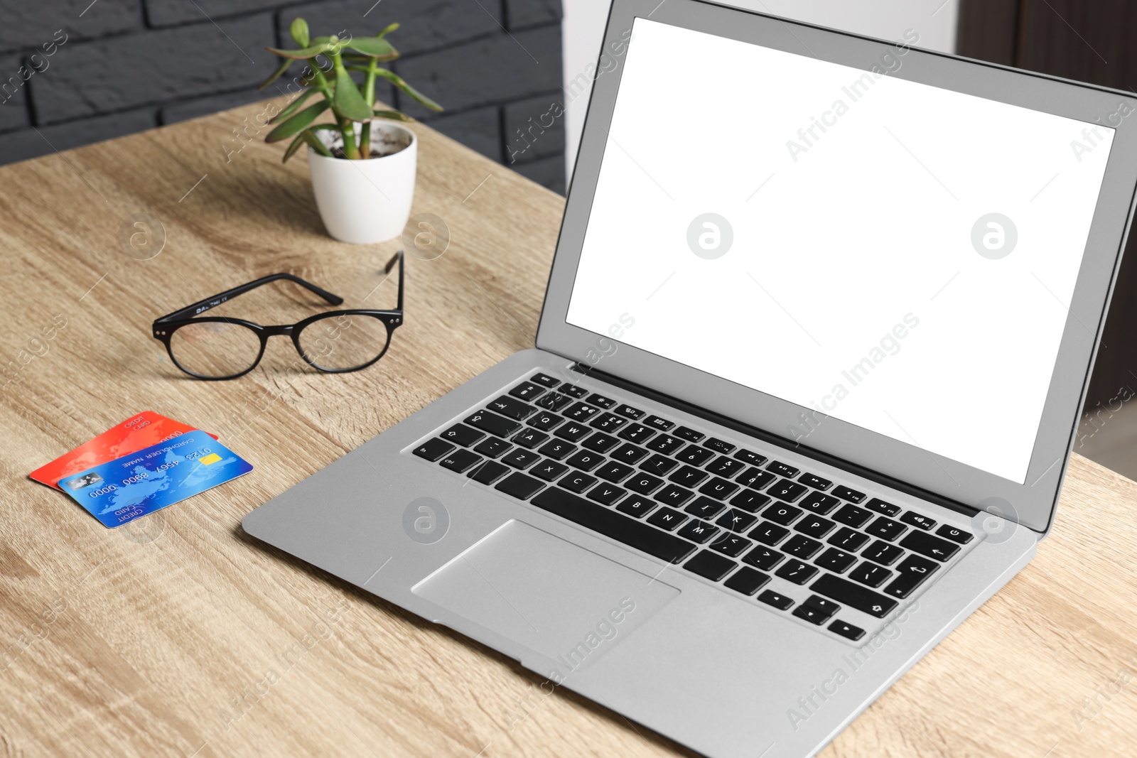 Photo of Laptop with blank screen and credit cards on wooden table indoors