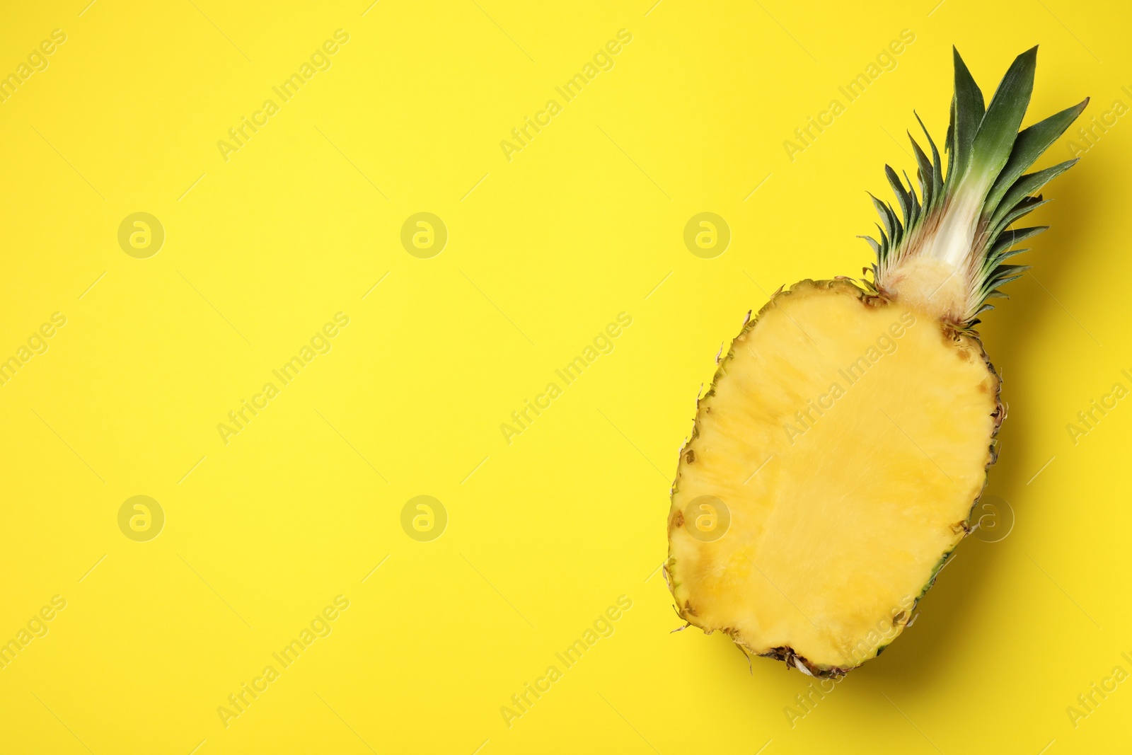 Photo of Half of fresh pineapple on yellow background, top view. Space for text