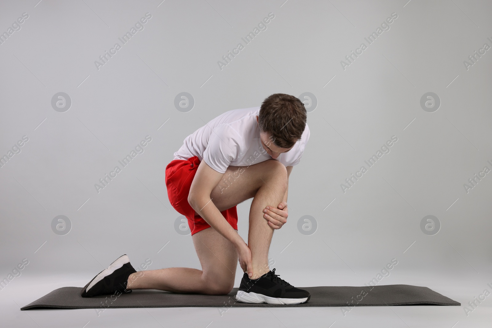 Photo of Man suffering from leg pain on mat against grey background