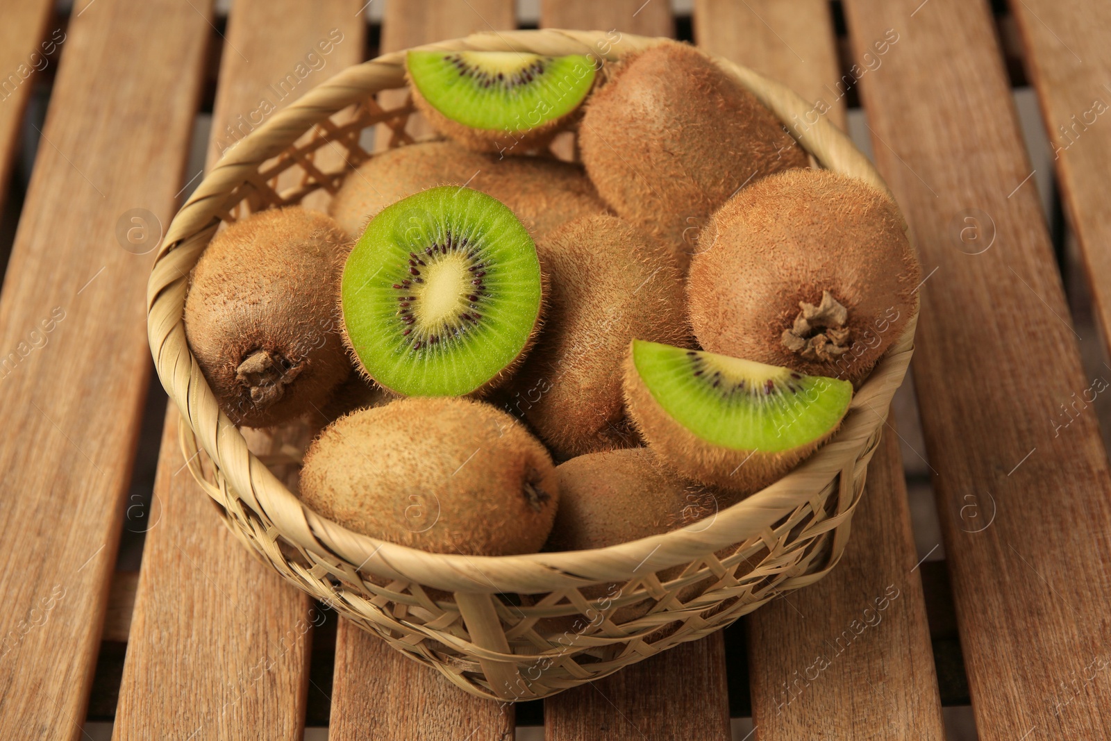Photo of Wicker basket with whole and cut kiwis on wooden table, closeup