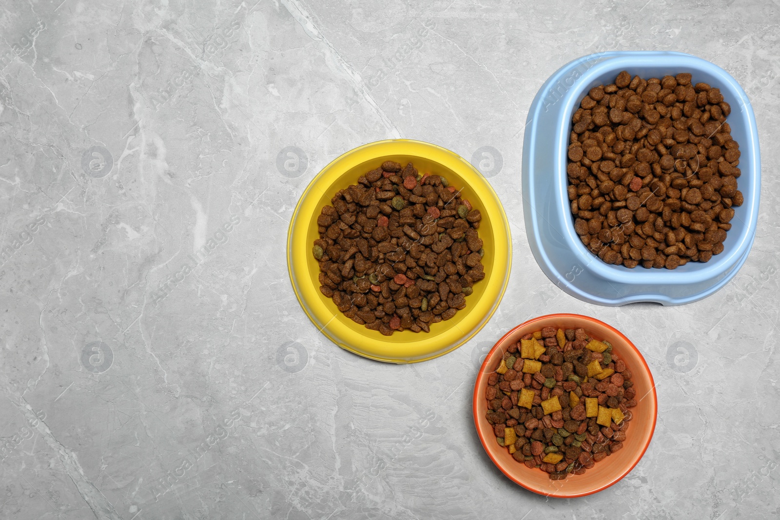 Photo of Pet bowls with dry food on light grey background, flat lay. Space for text