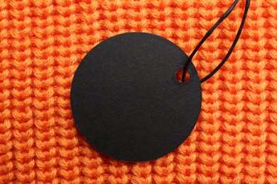 Circle shaped tag with space for text on orange knitted background, top view