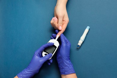 Diabetes. Doctor checking patient's blood sugar level with glucometer on blue background, top view