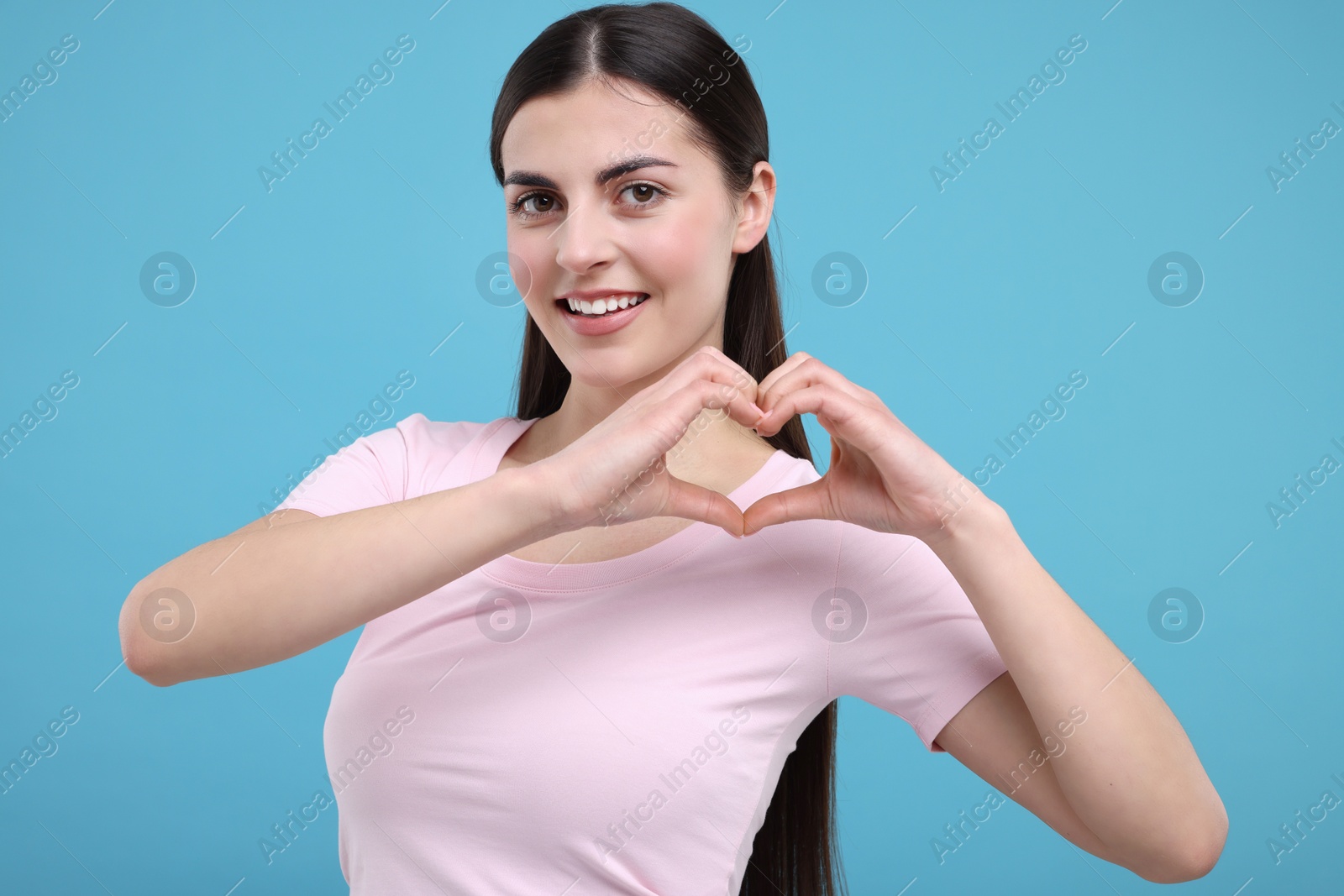 Photo of Beautiful young woman making heart with hands on light blue background