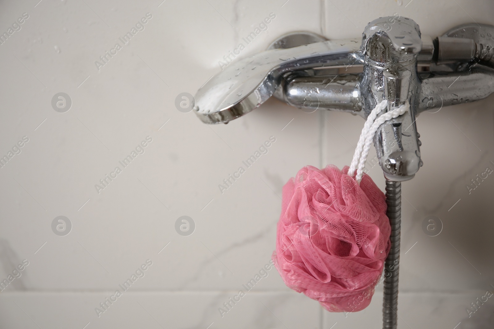 Photo of Pink shower puff hanging on faucet in bathroom, space for text