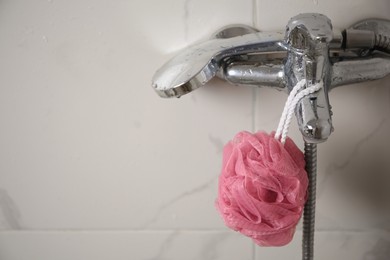 Photo of Pink shower puff hanging on faucet in bathroom, space for text