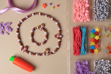 Handmade jewelry kit for kids. Colorful beads, necklace, bracelet and ribbon on beige background, flat lay