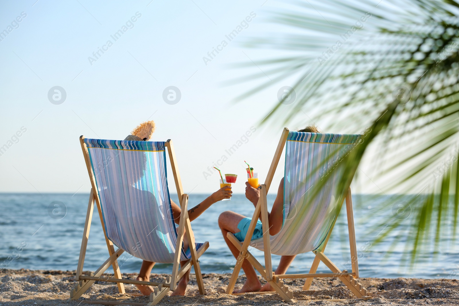 Photo of Young couple with cocktails in beach chairs at seacoast