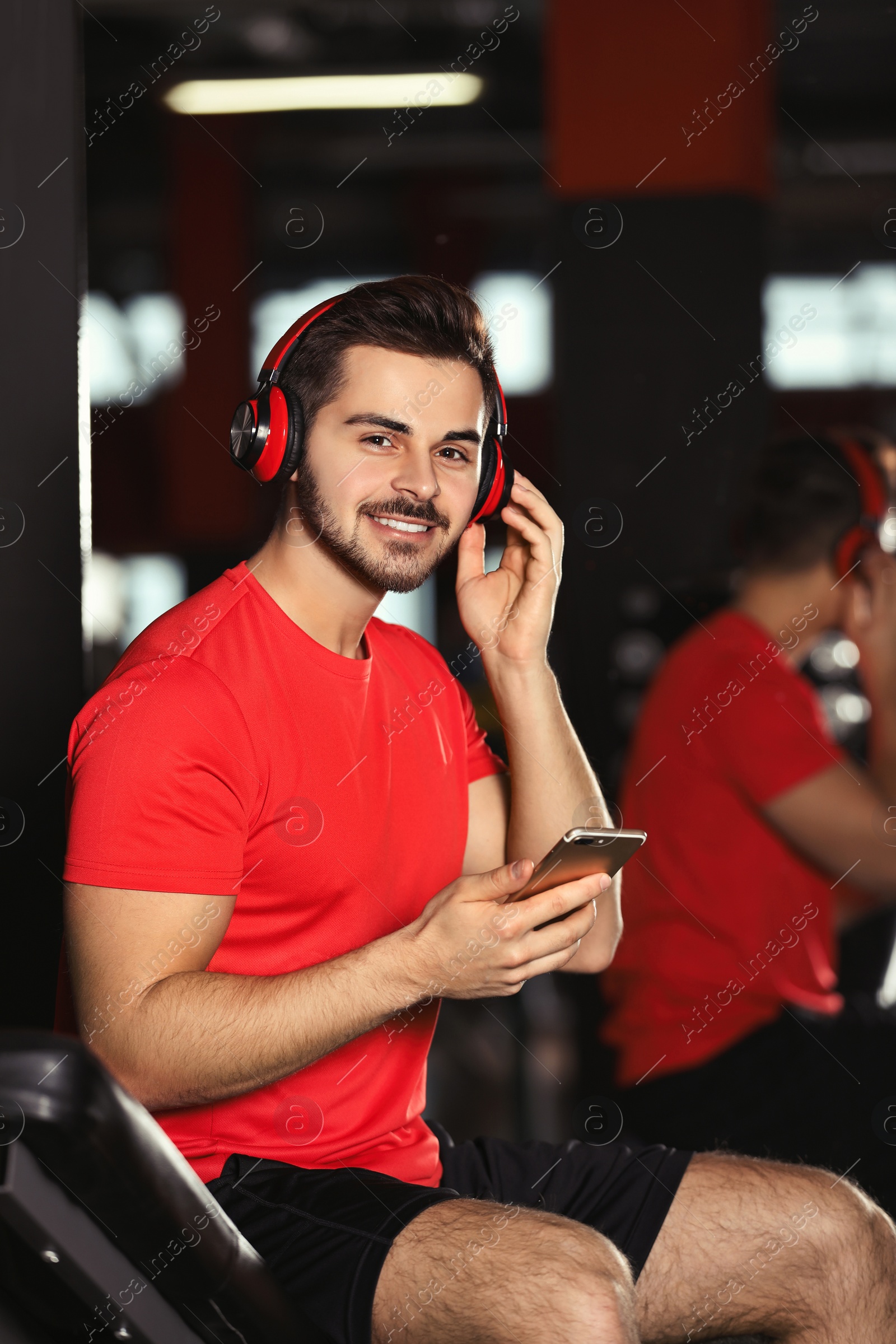 Photo of Young man with headphones listening to music on mobile device at gym