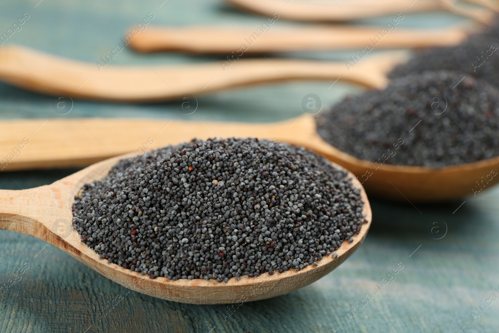 Photo of Poppy seeds in spoons on blue wooden table, closeup