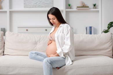 Beautiful pregnant woman sitting on sofa at home