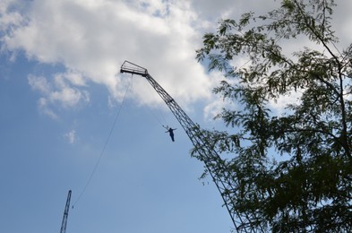 Amusement park. Person jumping from tower against blue sky, low angle view