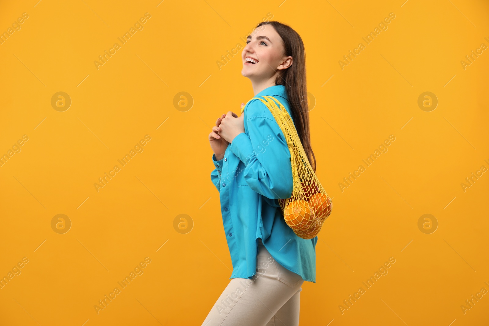 Photo of Woman with string bag of fresh oranges on orange background