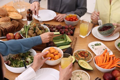 Friends eating vegetarian food at wooden table indoors, closeup