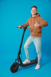 Photo of Happy man with modern electric kick scooter showing thumbs up on light blue background