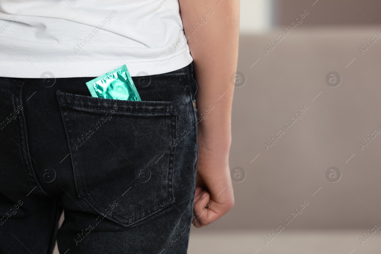 Photo of Teenage boy with condom in pocket of his jeans indoors, closeup. Sex education concept