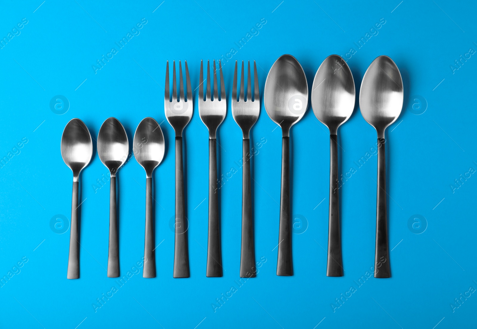 Photo of New spoons and forks on blue background, flat lay