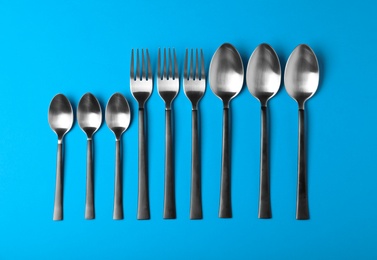 Photo of New spoons and forks on blue background, flat lay