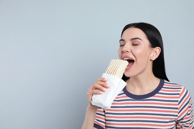 Photo of Young woman eating delicious shawarma on grey background. Space for text