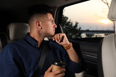 Photo of Thoughtful man with cup of drink in modern taxi