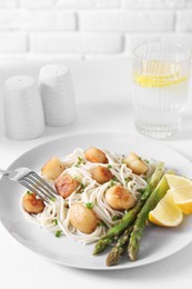 Photo of Delicious scallop pasta with asparagus, green onion and lemon served on white table, closeup