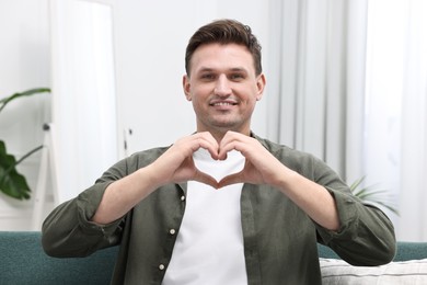 Photo of Happy man making heart with hands at home