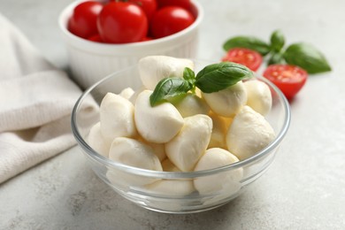 Delicious mozzarella balls and basil leaves in glass bowl on light gray table, closeup