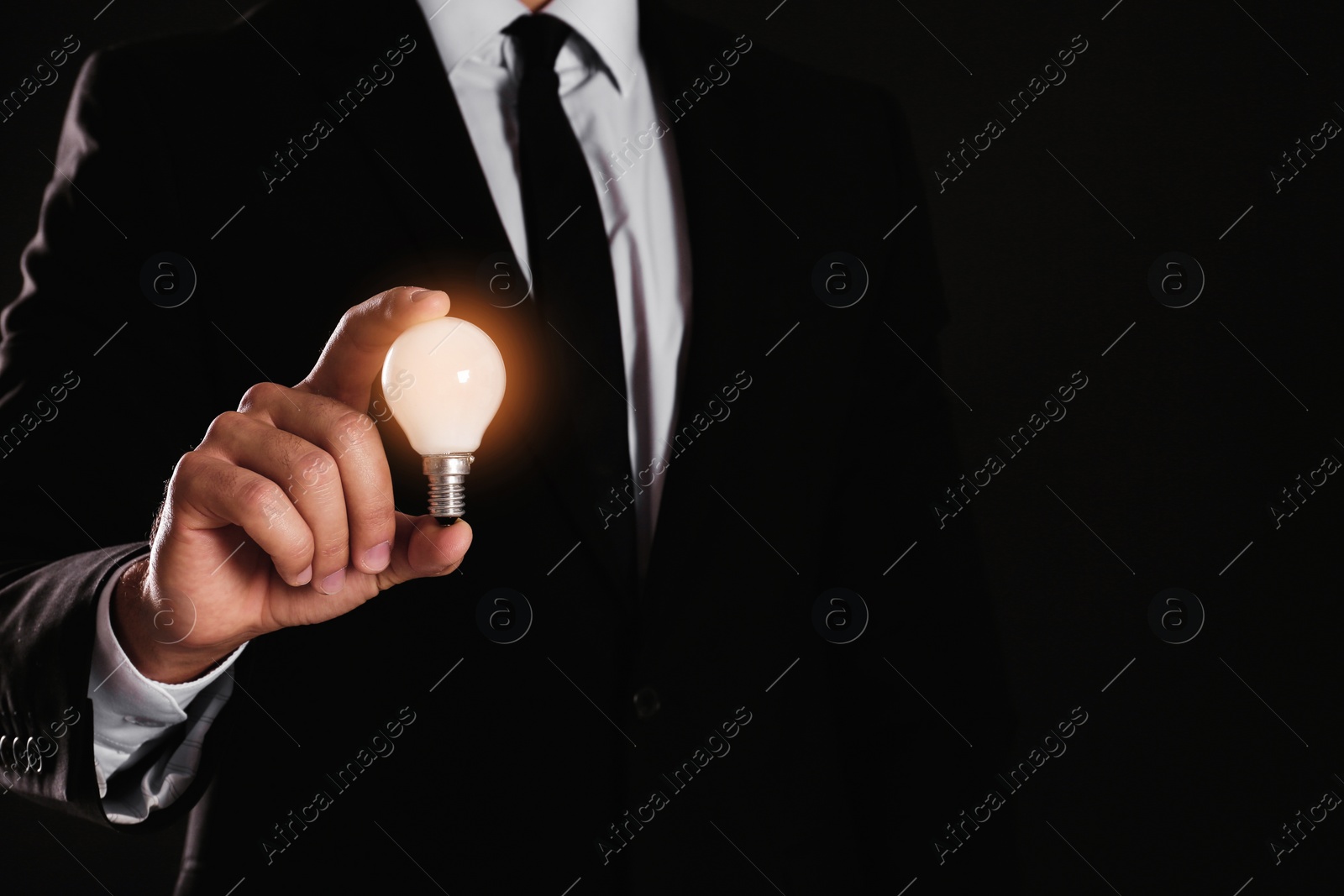 Photo of Businessman holding lamp bulb against dark background, closeup. Space for text