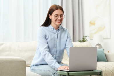 Smiling woman in stylish eyeglasses working with laptop at home