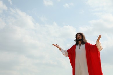 Photo of Jesus Christ raising hands against blue sky. Space for text