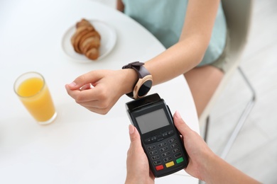 Photo of Woman using smart watch for contactless payment via terminal in cafe, closeup