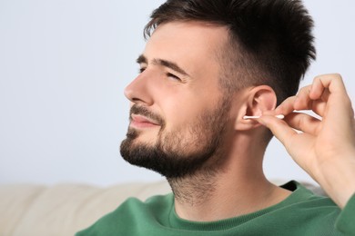 Young man cleaning ear with cotton swab at home