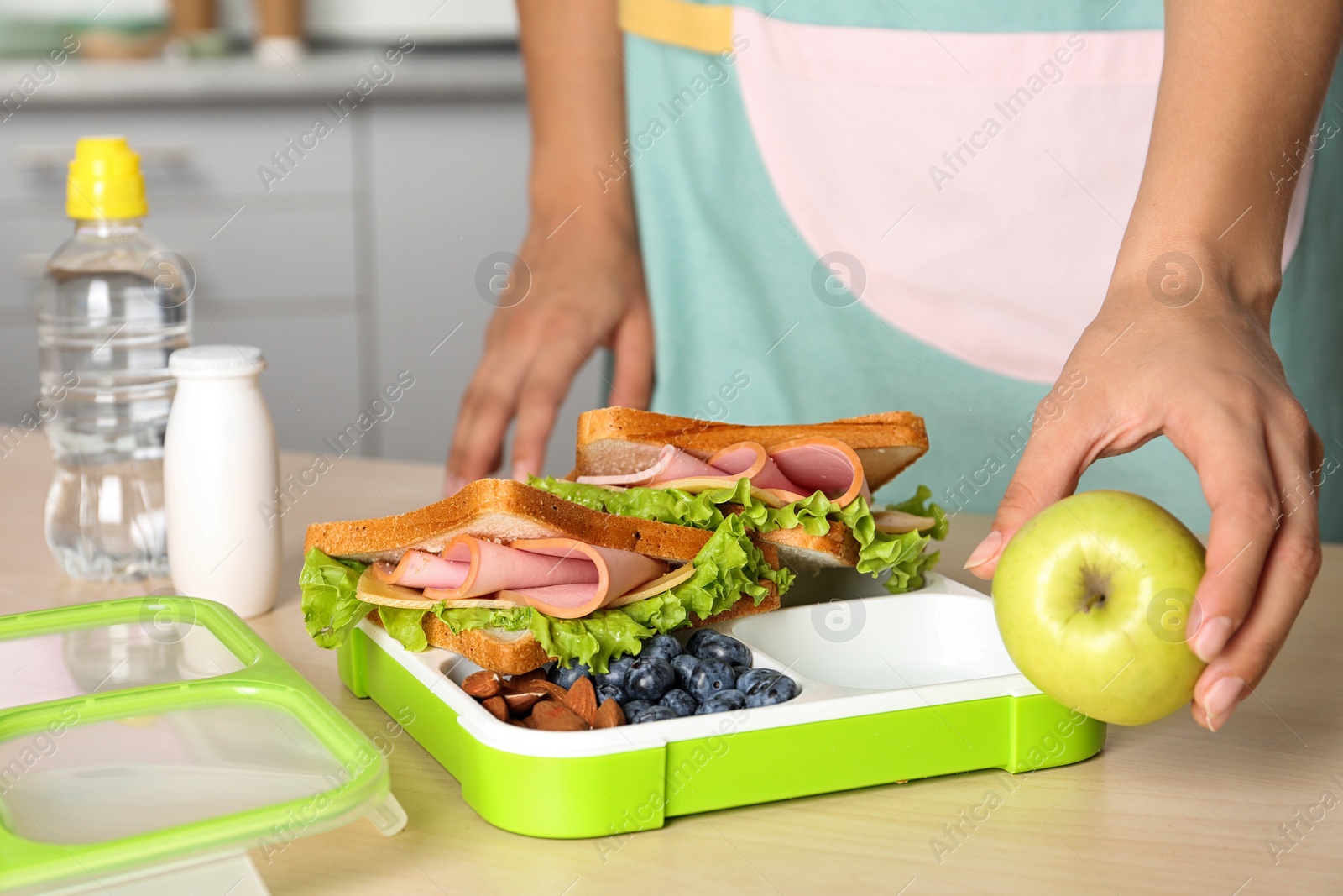 Photo of Woman preparing food for her child at table in kitchen, closeup. Healthy school lunch