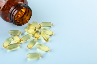 Bottle and vitamin capsules on light blue background, closeup. Space for text