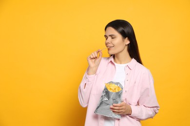 Beautiful woman eating potato chips on orange background, space for text