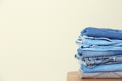 Photo of Stack of different jeans on table against light background. Space for text