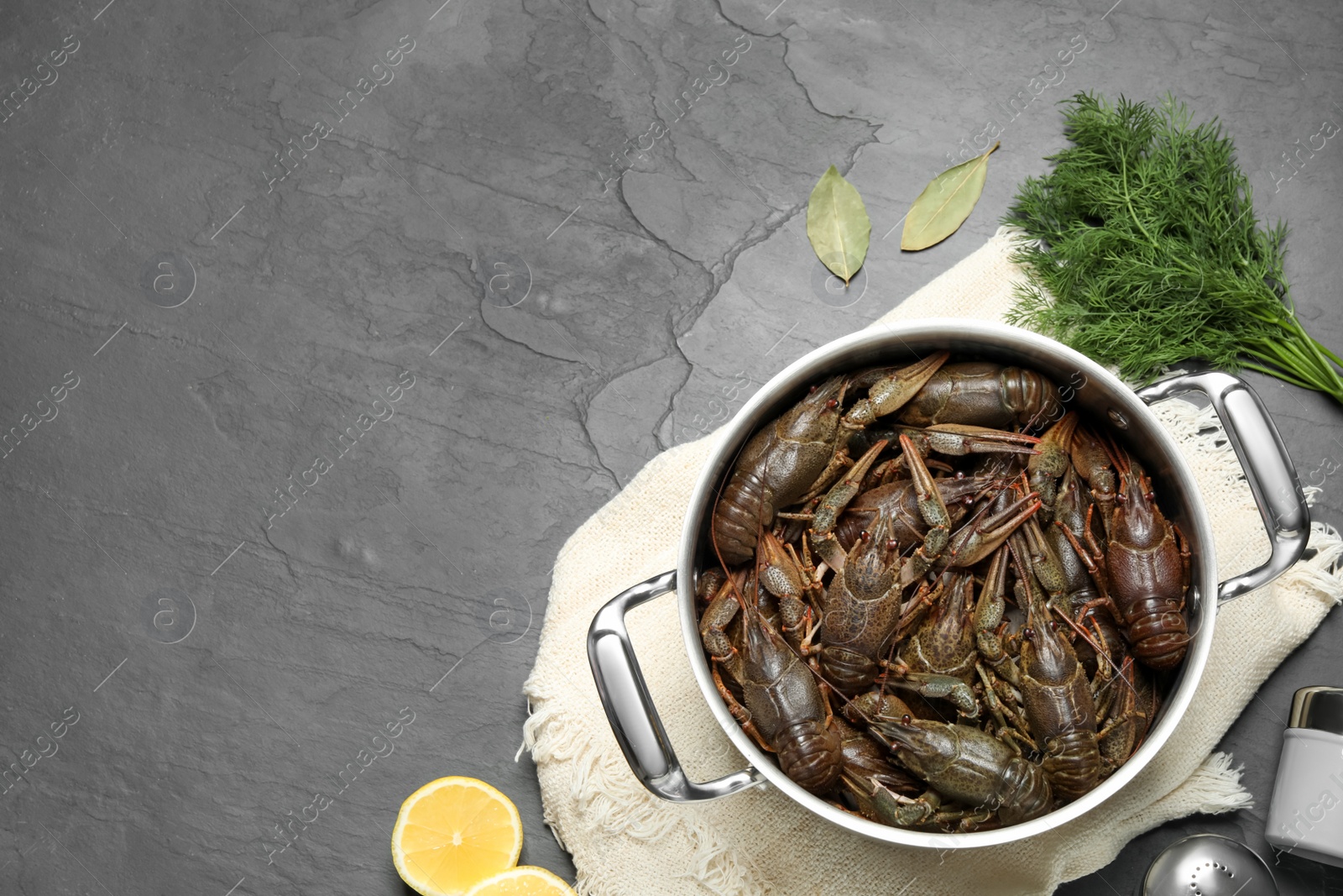 Photo of Fresh raw crayfishes in pot on black table, flat lay. Space for text