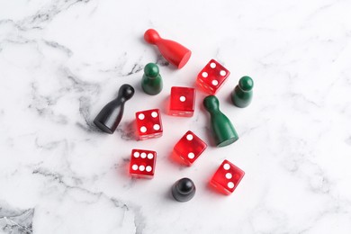 Photo of Red dices and game pieces on white marble table, flat lay