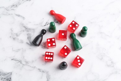 Red dices and game pieces on white marble table, flat lay