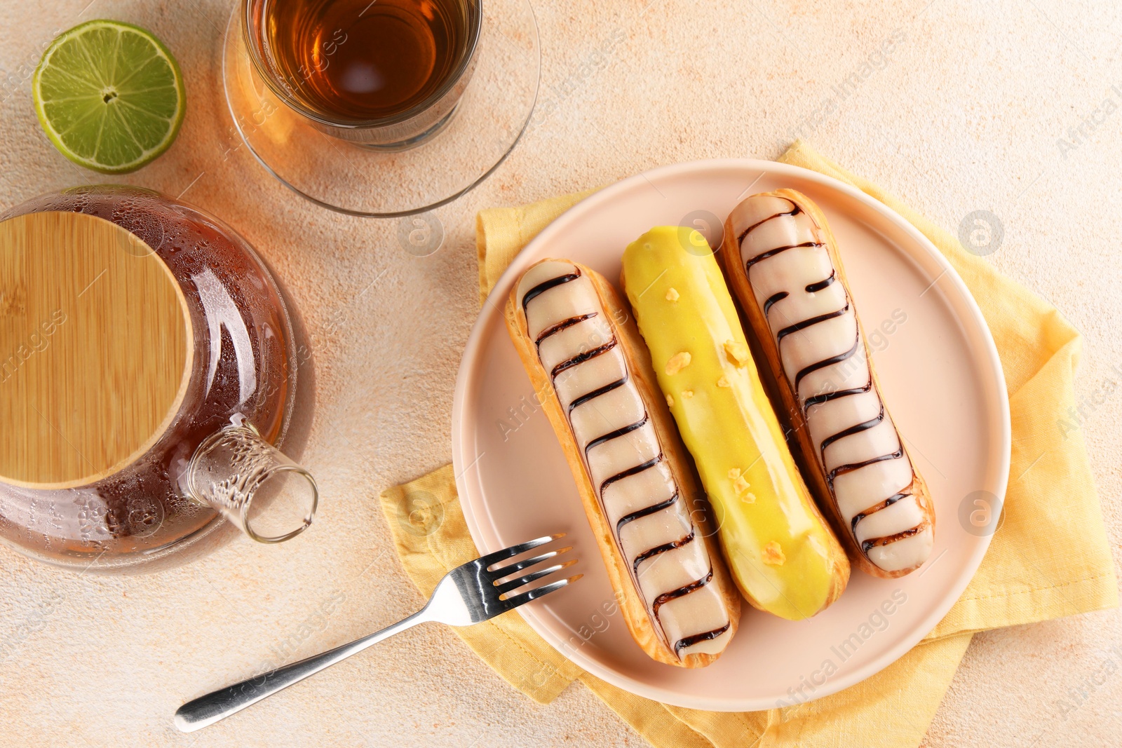 Photo of Different tasty glazed eclairs and tea served on color textured table, flat lay