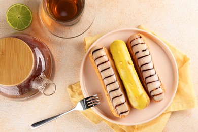 Different tasty glazed eclairs and tea served on color textured table, flat lay