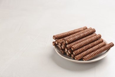 Plate with delicious chocolate wafer rolls on white table, space for text. Sweet food